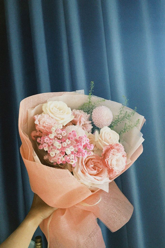 A beautiful bouquet featuring pink roses, carnations, and other flowers against a blue backdrop.