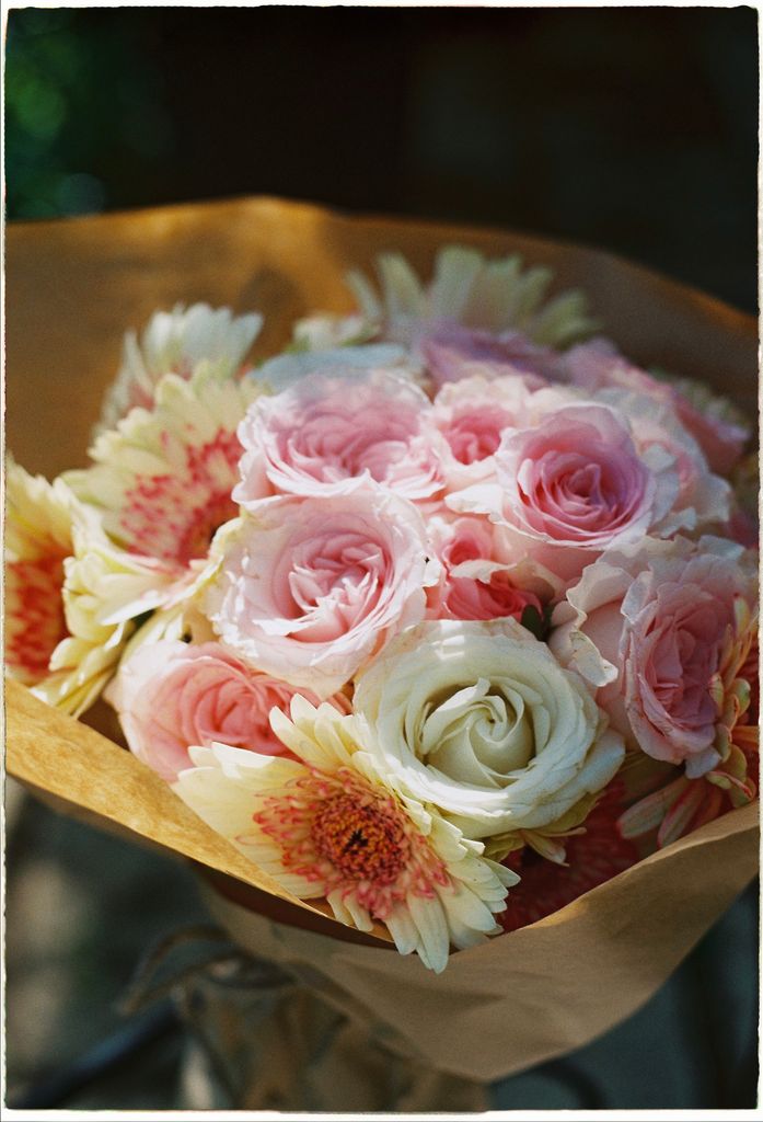 A beautiful bouquet of pink roses and daisies wrapped in paper, perfect for romantic occasions.