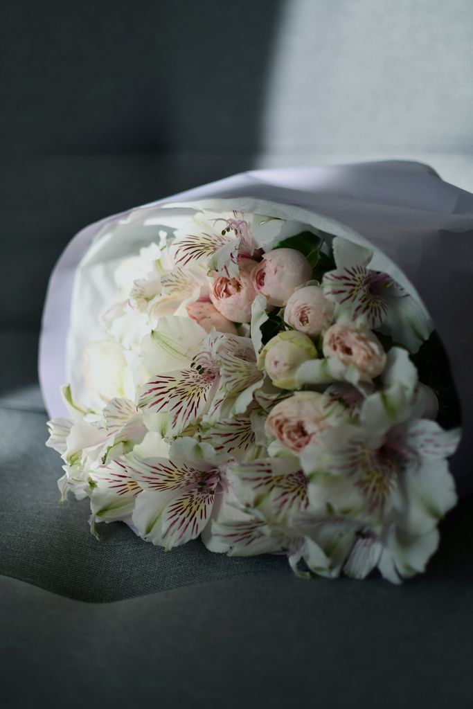 A close-up shot of a beautiful bouquet of alstroemeria and roses wrapped in white paper.