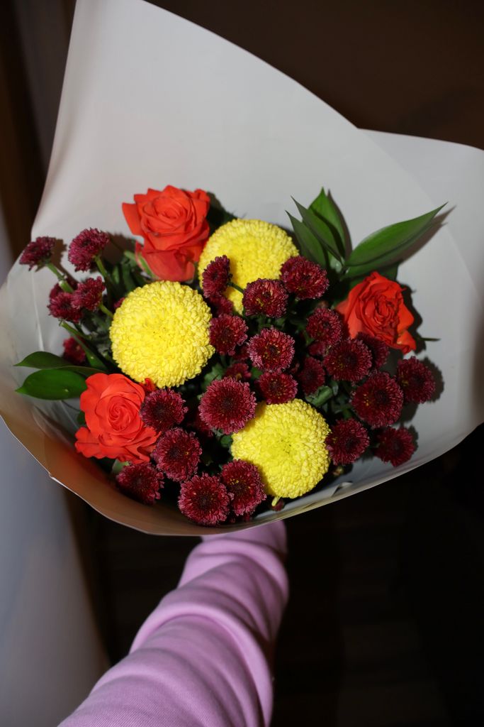 A colorful bouquet featuring red roses and yellow chrysanthemums wrapped in white paper.