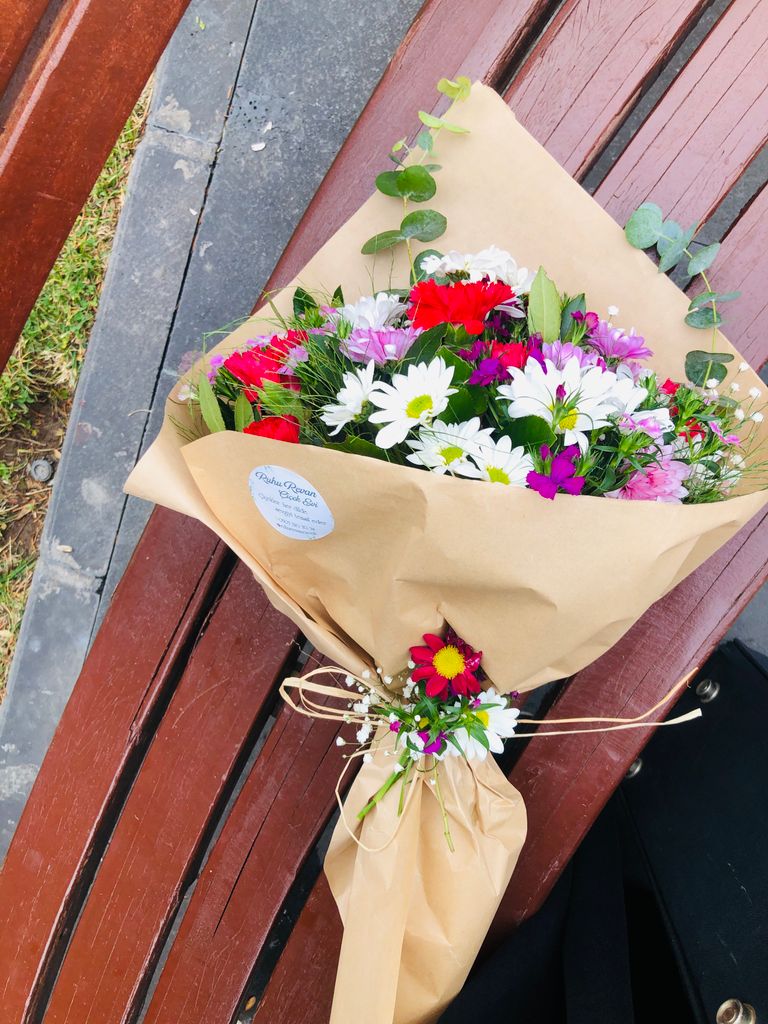 Vibrant flower bouquet wrapped in paper placed on a classic wooden bench.